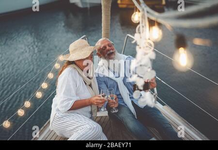 Senior couple toasting champagne while taking selfie on sailboat vacation - Happy mature people having fun celebrating wedding anniversary on boat Stock Photo