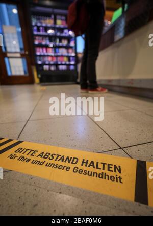 27 March 2020, Saxony, Leipzig: A woman is standing behind a warning sticker asking for distance at the checkout in a supermarket. Grocery stores are open despite contact restrictions. Protective walls and safety notices are to protect employees and customers from the corona virus. Photo: Jan Woitas/dpa-Zentralbild/dpa Stock Photo