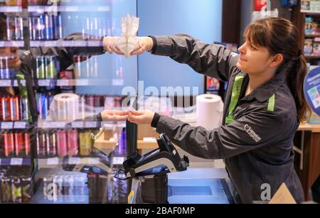 27 March 2020, Saxony, Leipzig: An employee of a 'Konsum' supermarket cleans a pane of Plexiglas, which was attached to the cash register to protect against infection with the corona virus. Grocery stores are open despite the contact restrictions. Protective walls and safety notices are intended to protect employees and customers from the corona virus. Photo: Jan Woitas/dpa-Zentralbild/dpa Stock Photo