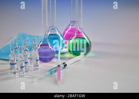 Four medical flasks with colorful chemical reagents. Seven mockup ampoules with transparent liquid, syringes and mask isolated on white. Laboratory re Stock Photo