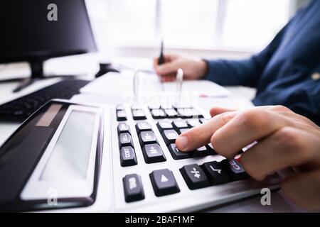Young Businessman Calculating Bill With Computer And Laptop On Desk Stock Photo