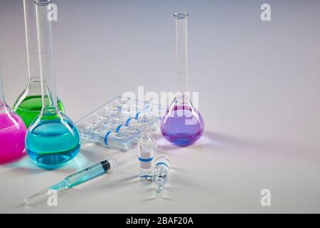 Four medical flasks with colorful chemical reagents. Seven mockup ampoules with transparent liquid and syringe isolated on white. Laboratory research Stock Photo
