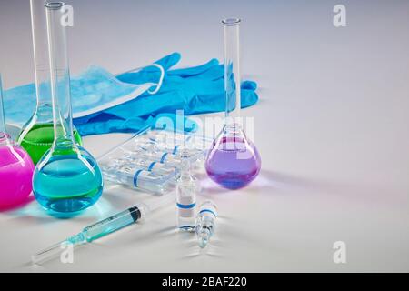 Four medical flasks with colorful chemical reagents. Seven mockup ampoules with liquid, syringe, blue disposable gloves and mask isolated on white. Co Stock Photo