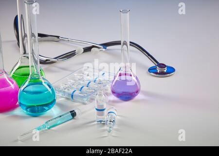 Four medical flasks with colorful chemical reagents. Seven mockup ampoules with transparent liquid, syringe and phonendoscope isolated on white. Labor Stock Photo