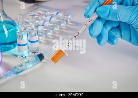Hands in blue disposable gloves holding testing kit. Medical flasks with colorful chemical reagents. Ampoules with liquid and syringe isolated on whit Stock Photo