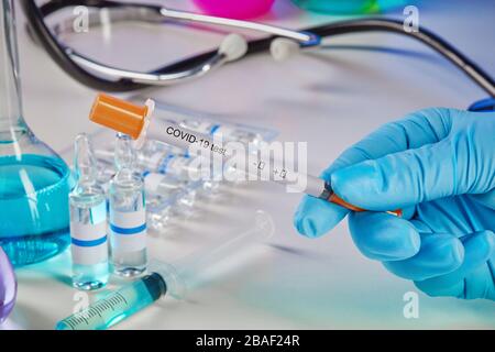 Hands in disposable gloves holding testing kit. Medical flasks, colorful chemical reagents. Ampoules with liquid, syringe, phonendoscope isolated on w Stock Photo