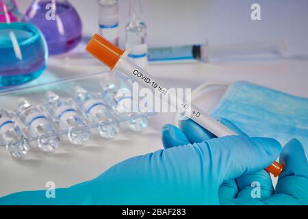 Hand in blue disposable glove holding testing kit. Medical flasks with colorful chemical reagents. Ampoules with liquid , mask and syringe isolated on Stock Photo