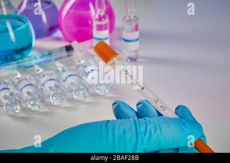 Hand in blue disposable glove holding testing kit. Medical flasks with colorful chemical reagents. Ampoules with liquid and syringe isolated on white. Stock Photo