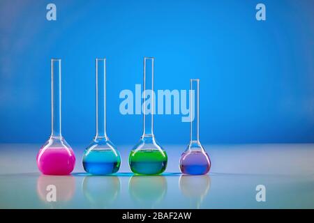 Four medical flasks with colorful chemical reagents for tests, blue background. Laboratory research of Coronavirus. Worldwide pandemic COVID-19, 2019- Stock Photo
