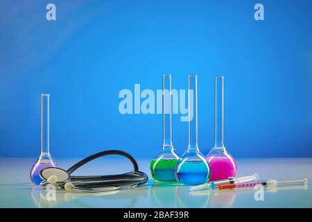 Four medical flasks with colorful chemical reagents. Testing kit, syringe and phonendoscope, blue background. Laboratory research Coronavirus. Worldwi Stock Photo