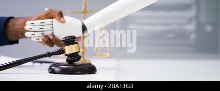 Gavel In Front Of Businessperson And Robot Shaking Hands Stock Photo