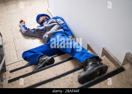 Unconscious Handyman Lying On Staircase With Helmet On Floor Stock Photo