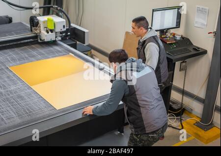 Two printshop worker technicians works on large CNC computer numerical control printing and cutting machine Stock Photo