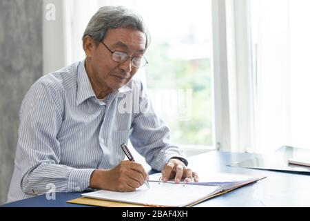 Asian smart business elder writing document report in the office. Stock Photo