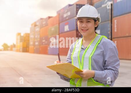 Asian young teen happy worker checking stock in shipping port work manage import export cargo containers. Stock Photo