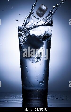 Glass of water with splash and ice on  blue background. Stock Photo