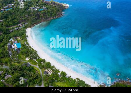 Aerial drone view of Anse Petite curved turquoise bay with beach resort, white sand and tropical hillside, Mahe, Seychelles Stock Photo