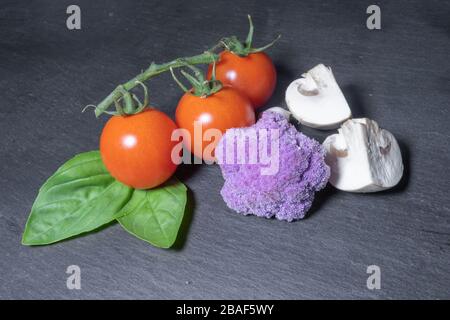 Red cherry tomatoes and green basil leaves on dark background with purple cauliflower Stock Photo