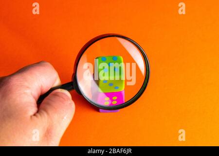 Hand holds magnifying glass over playing cubes. The focus is on the green cube. Search casinos, gambling, fortune Stock Photo