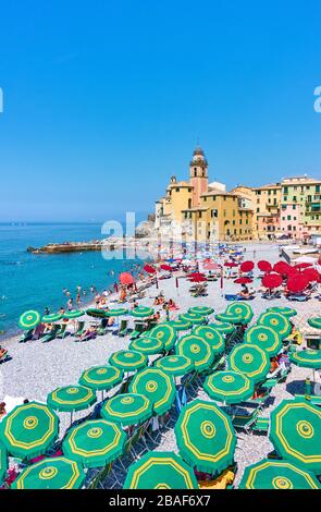 Camogli, Genoa, Italy - July 3, 2019:  Beach with umbrellas and resting people near old church in Camogli, Genova Stock Photo