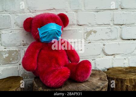 Lonely Red Teddy bear in a protective medical mask on a yellow background with respiratory masks. Coronavirus covid-19 prevention concept. Stock Photo