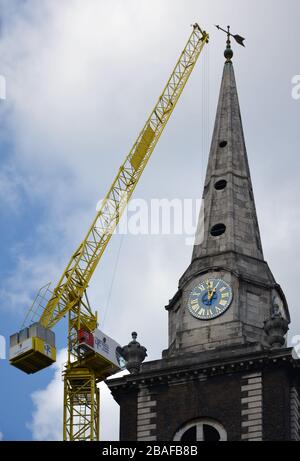 The bell tower and spire of the St Botolph without Aldgate church, with a crane from a nearby construction site,looking closer to the spire than it ac Stock Photo