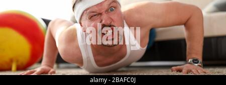 Funny grimacing man making push-ups home Stock Photo