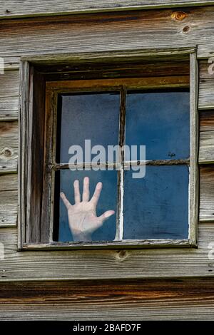 Vertical shot of a four paned window in a wooden wall with a woman's hand pressed against one pane as if trying to escape. Stock Photo