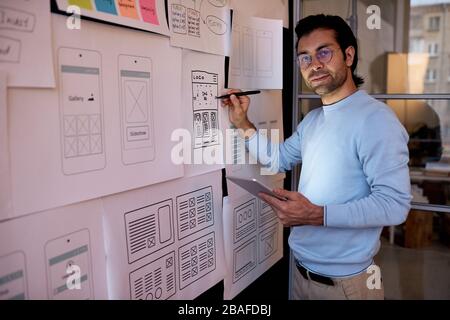 Portrait of handsome user interface designer with stubble standing at planning board and working on new app design Stock Photo