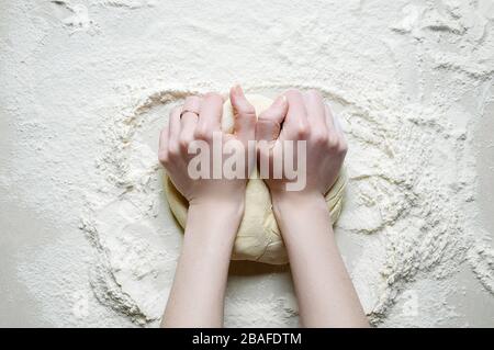 Woman Hands Kneads the Dough with Flour on the White Kitchen Table. Top View Flat Lay. Copy Space for Your Text. Stock Photo