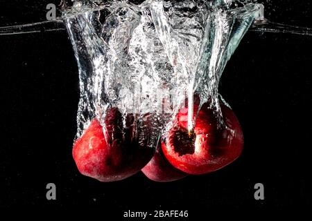 Closeup shot of red apples falling deeply under the water and making a splash Stock Photo
