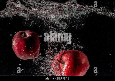 Closeup shot of red apples falling deeply under the water and making a splash Stock Photo