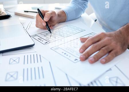 Close-up of unrecognizable UI engineer sitting at desk and making interface design for device Stock Photo
