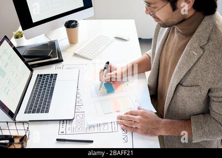 Busy man in stylish jacket sitting at desk drawing on phone schemes while developing icon placement Stock Photo