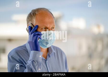 A man using protective masks and blue latex gloves while using mobile phone in urban scenery Stock Photo