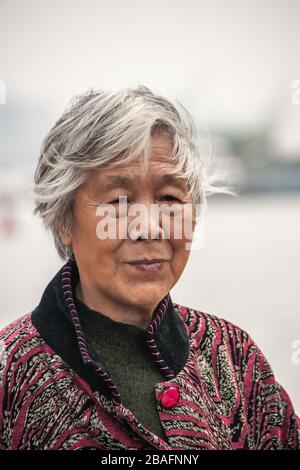 Shanghai, China - May 4, 2010: Closeup of face of older graying senior woman with cloths featuring blacks, pinks and grays. Stock Photo