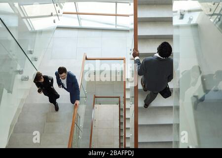 Overview of three young intercultural office workers in formalwear going upstairs while hurrying for work in the morning Stock Photo