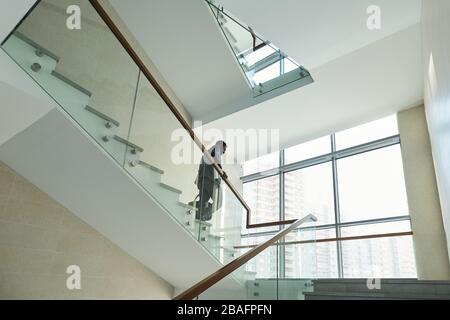 Young African male office worker in formalwear moving downstairs after work while holding by banisters inside large business canter Stock Photo