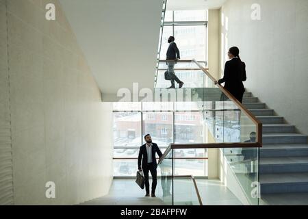 Three young contemporary managers of large office center going upstairs while hurrying for work in the morning or after lunch break Stock Photo
