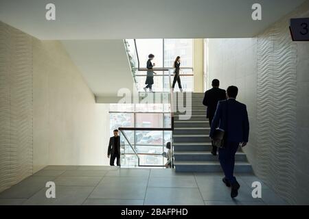 Large group of young contemporary office managers going upstairs and downstairs in the middle of working day in business center Stock Photo
