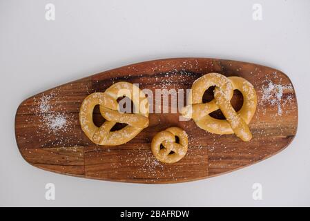 Three soft pretzels on a wooden cutting board sprinkled with salt against a white background. Stock Photo