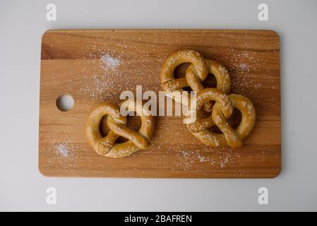 Three soft pretzels on a wooden cutting board sprinkled with salt against a white background. Stock Photo