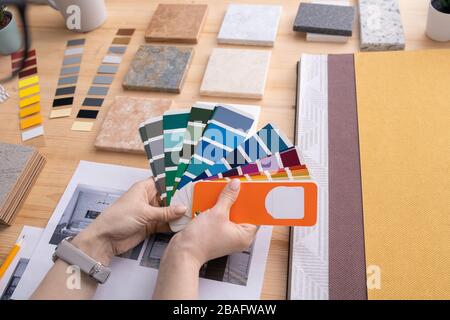 Hands of young female creative designer holding color palette with swatches over table with samples of panels and wallpapers Stock Photo