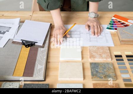 Hands of young creative female designer or architect with pencil standing by wooden table while working with sketches on paper Stock Photo