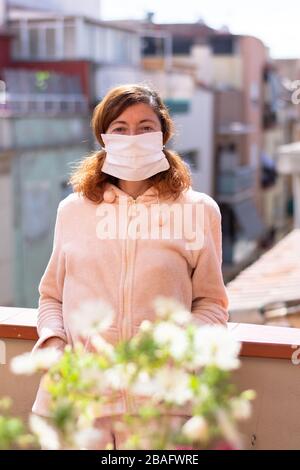 Woman with mask confined at home taking air on the terrace, measures against Coronavirus, COVID 19 Stock Photo