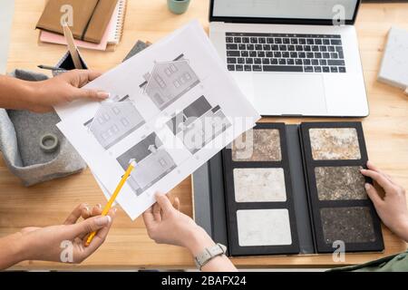 One of young female designers or architects holding papers with house sketches while her colleague pointing at one of them Stock Photo