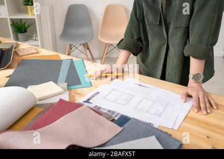 Young creative female designer in casualwear standing by table and working with house sketch on paper in studio Stock Photo