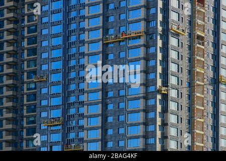 Facade of a house under construction. Installation of windows. Builders work on special suspended platforms. Background Stock Photo