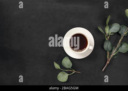 Cup of coffee and leaves on black background. Flat lay, top view, copy space. Stock Photo