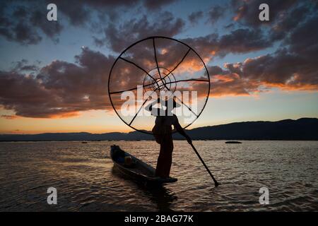 Burmese fisherman on bamboo boat catching fish in traditional way with handmade net. Inle lake, Myanmar (Burma) travel destination Stock Photo